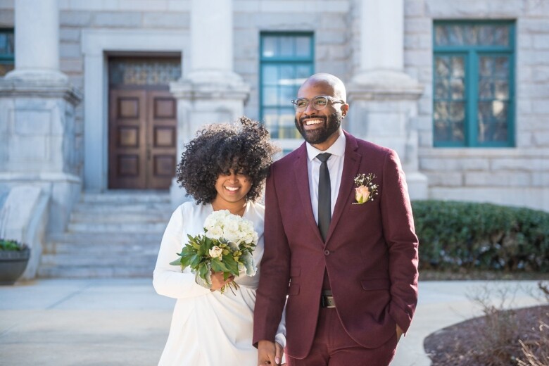 Bride in a white gown and groom in a burgundy suit outside the Historic DeKalb Courthouse
