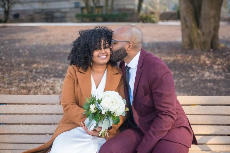 Newlyweds sharing a kiss on a park bench, the bride holding a white rose bouquet