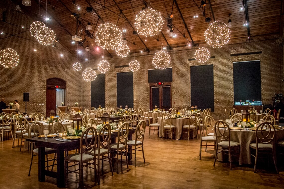 Charles H. Morris Center ballroom in Savannah set for a wedding reception, with exposed brick walls, a wood-beamed ceiling and hanging globe string lights